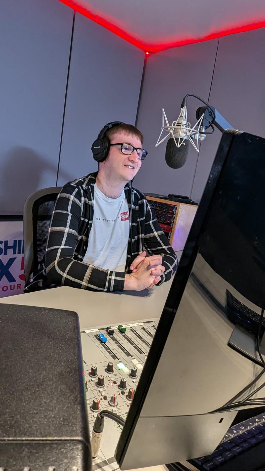 Adam sits in the radio studio, with the mic hanging in front of him and wearing headphones