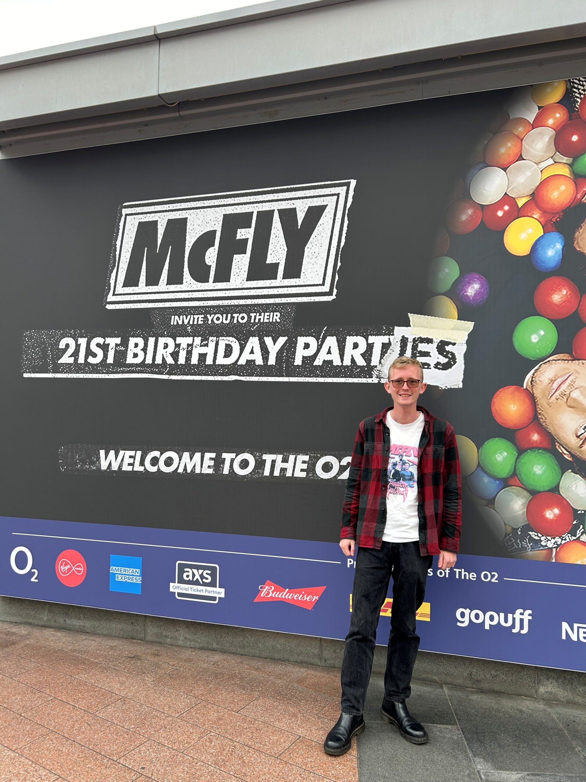 James stands in casual clothing in front of a McFly billboard
