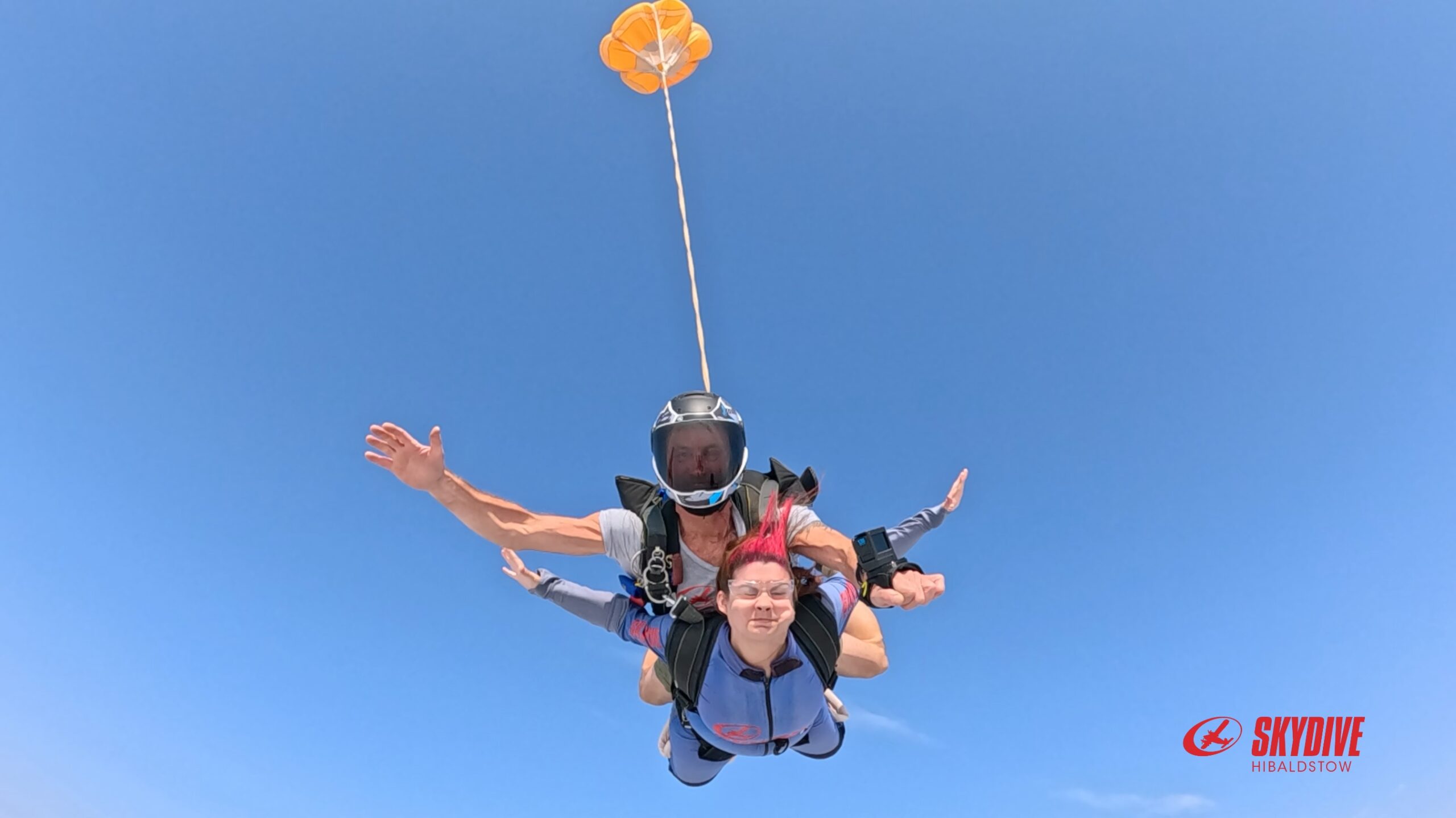 Skydive 1 A photo taken from below of Millie skydiving with an instructor against a bright blue sky.